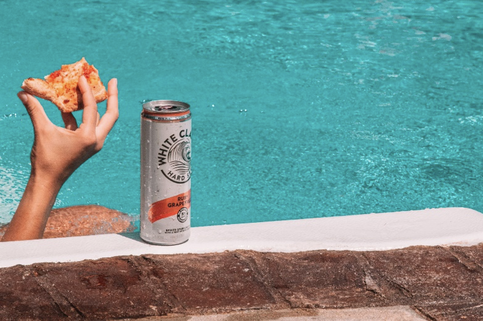 BevAlc trends hard seltzers drinking whiteclaw by pool with pizza in hand